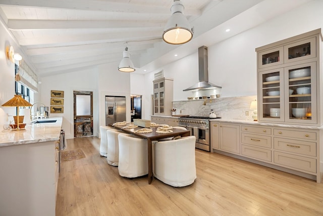 kitchen featuring wall chimney exhaust hood, sink, vaulted ceiling with beams, light stone counters, and appliances with stainless steel finishes