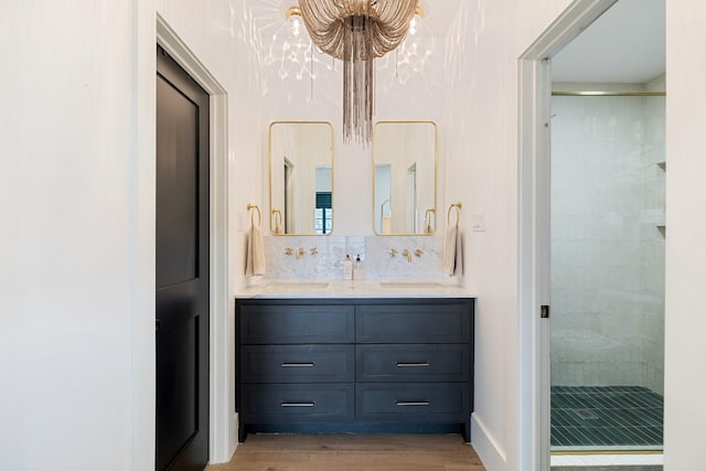 bathroom featuring an inviting chandelier, backsplash, hardwood / wood-style floors, tiled shower, and vanity