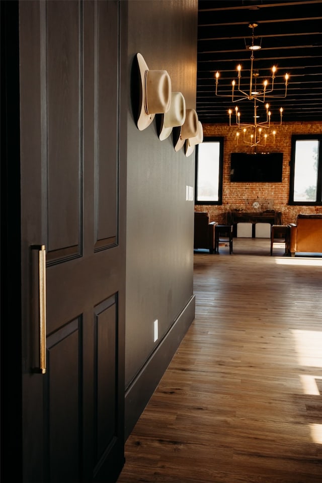 corridor featuring dark hardwood / wood-style floors, a chandelier, and brick wall