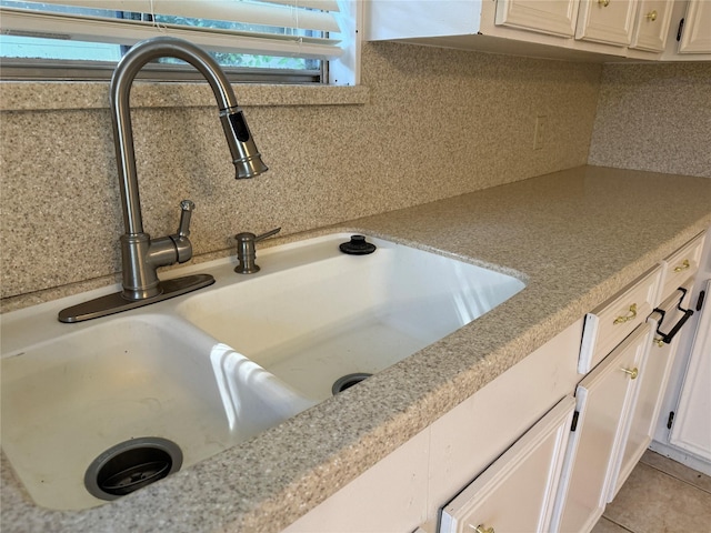 interior details featuring decorative backsplash, white cabinets, and sink