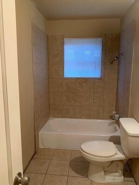 bathroom featuring tile patterned floors, tiled shower / bath combo, toilet, and a textured ceiling