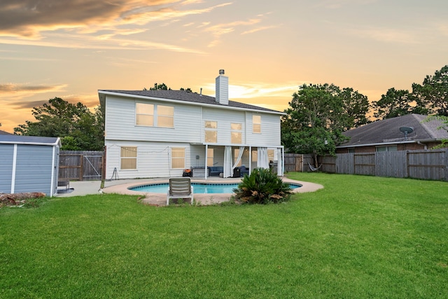 back house at dusk featuring a lawn, a patio area, and a fenced in pool