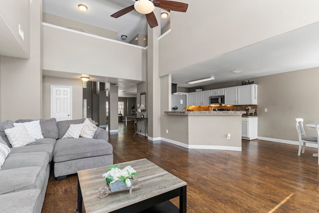 living room with ceiling fan, dark hardwood / wood-style floors, and a high ceiling