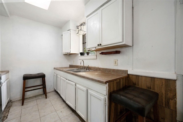 kitchen featuring wooden walls, sink, white cabinets, and light tile patterned flooring