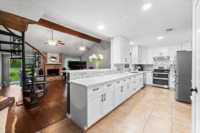 kitchen featuring lofted ceiling with beams, ceiling fan, appliances with stainless steel finishes, a fireplace, and light hardwood / wood-style floors