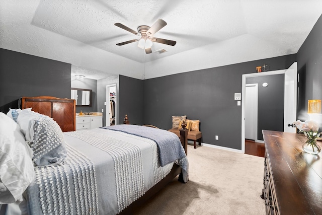 carpeted bedroom featuring a closet, a walk in closet, ceiling fan, and a tray ceiling