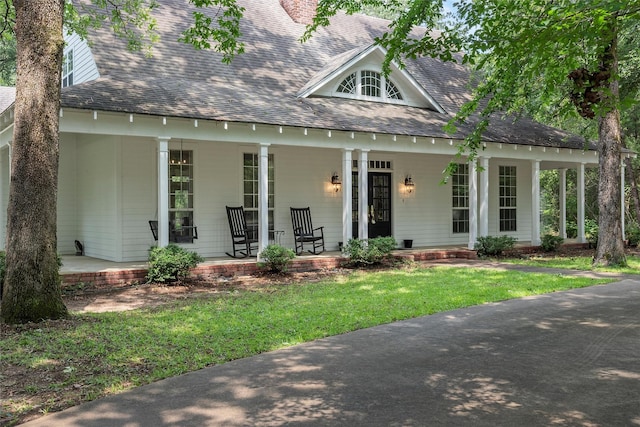 view of front of house with a porch, a chimney, a front lawn, and a shingled roof