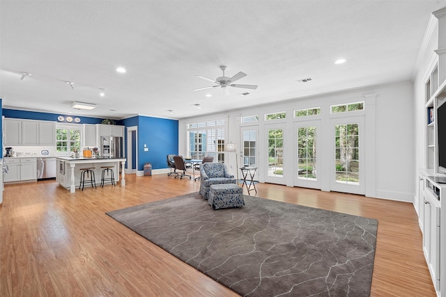 living room with a ceiling fan, visible vents, baseboards, and light wood-type flooring