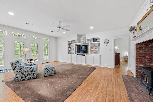 living room featuring wood-type flooring, built in features, a wood stove, and plenty of natural light