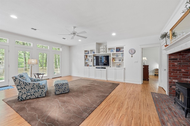 living area with light wood-style flooring, baseboards, a wood stove, and ceiling fan