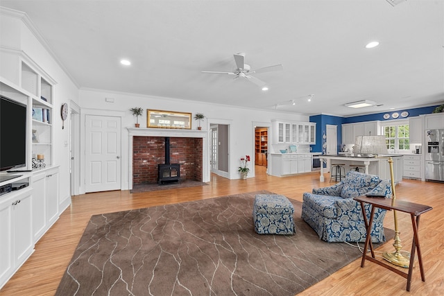 living room with ceiling fan, light hardwood / wood-style floors, a wood stove, and ornamental molding