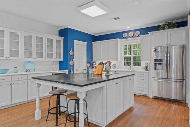 kitchen with white cabinetry, light hardwood / wood-style floors, stainless steel fridge, a kitchen island, and tasteful backsplash