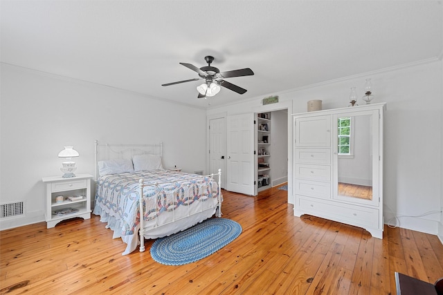 bedroom featuring baseboards, visible vents, light wood-style flooring, ceiling fan, and ornamental molding