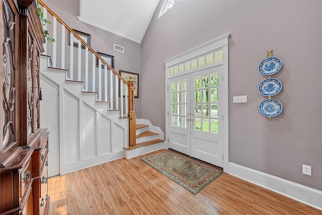 foyer with high vaulted ceiling, french doors, crown molding, and light wood-type flooring