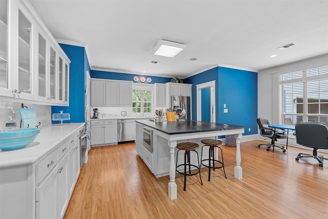 kitchen with light hardwood / wood-style floors, stainless steel appliances, a kitchen island, a kitchen bar, and white cabinetry