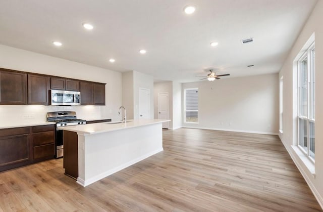 kitchen featuring ceiling fan, a center island with sink, sink, light wood-type flooring, and appliances with stainless steel finishes