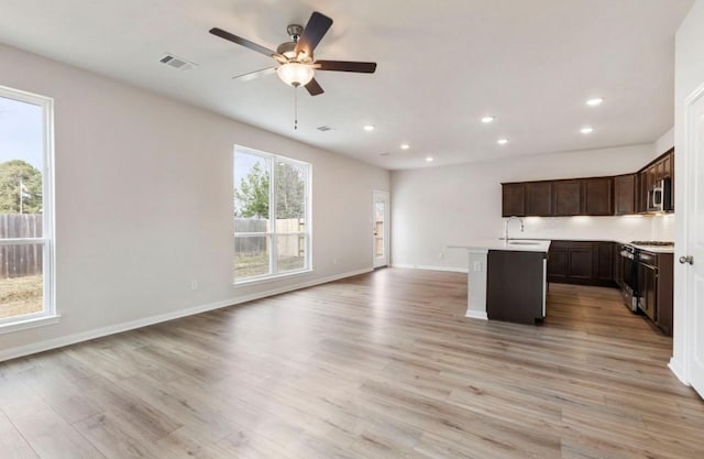 kitchen featuring a center island with sink, ceiling fan, stainless steel appliances, light wood-type flooring, and dark brown cabinets