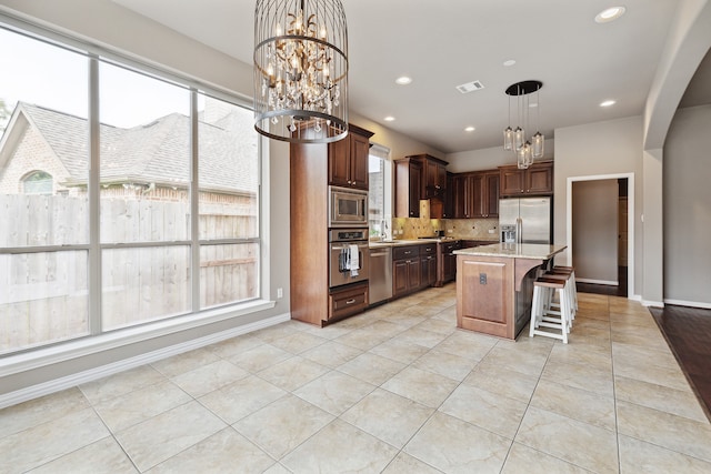 kitchen featuring stainless steel appliances, a kitchen breakfast bar, a notable chandelier, an island with sink, and pendant lighting