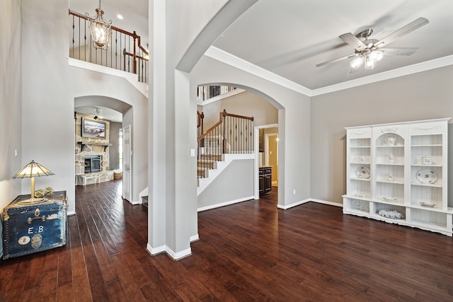 foyer entrance featuring dark hardwood / wood-style floors, ceiling fan, a stone fireplace, and crown molding