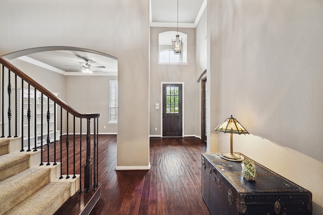 foyer entrance featuring a high ceiling, ceiling fan with notable chandelier, crown molding, and dark wood-type flooring