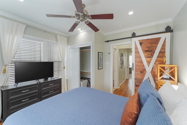 bedroom with crown molding, ceiling fan, a barn door, wood-type flooring, and a closet