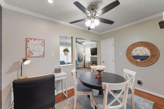 dining room with ceiling fan, crown molding, a textured ceiling, a fireplace, and hardwood / wood-style flooring