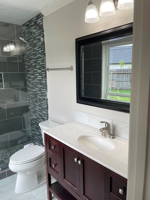 bathroom with tile patterned floors, vanity, a tile shower, and toilet