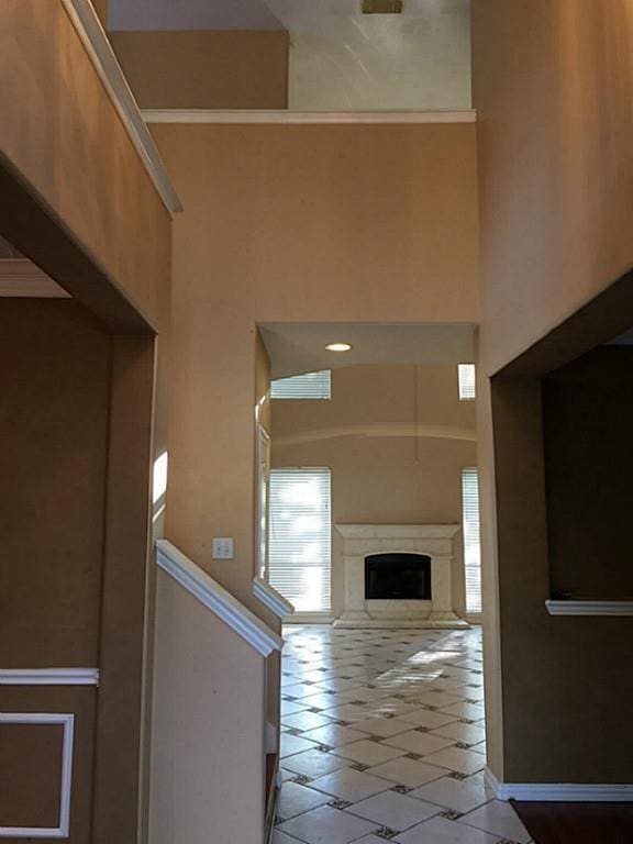 hall with a towering ceiling, crown molding, and light tile patterned floors