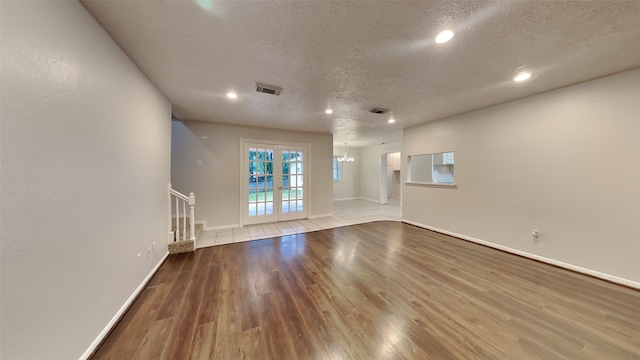 unfurnished living room with a notable chandelier, a textured ceiling, and light hardwood / wood-style flooring