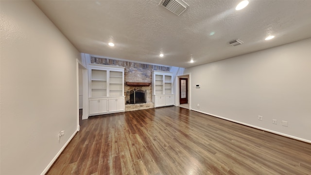 unfurnished living room featuring a fireplace, built in shelves, a textured ceiling, and hardwood / wood-style flooring