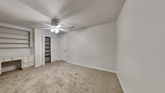 unfurnished bedroom with ceiling fan, light colored carpet, built in desk, and a textured ceiling