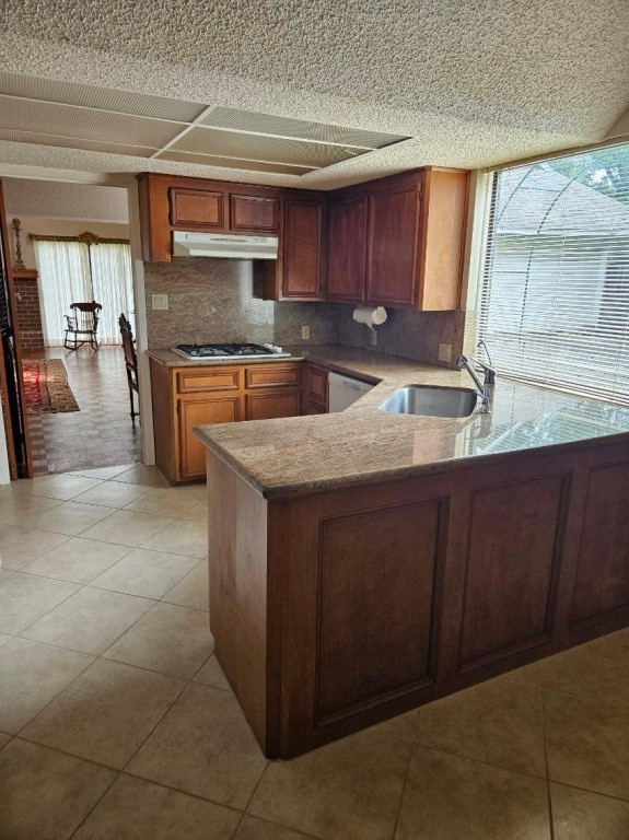 kitchen with light tile flooring, kitchen peninsula, backsplash, dishwasher, and sink