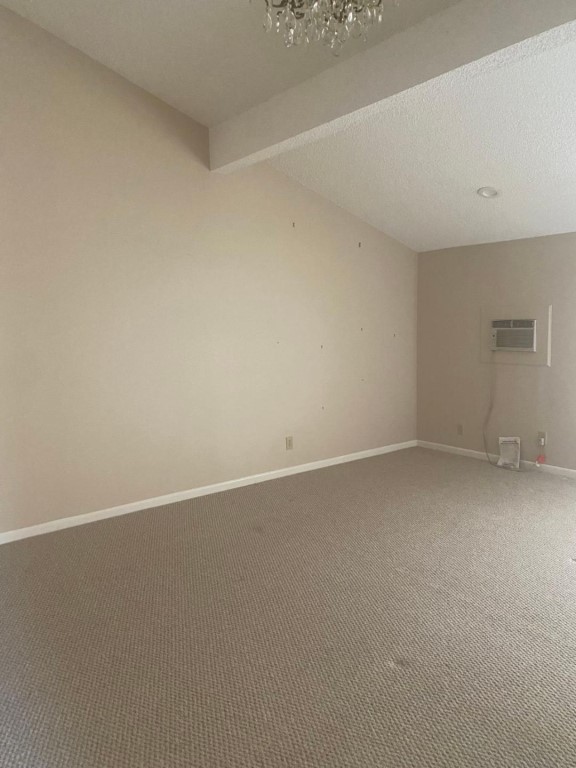 empty room with a wall unit AC, beam ceiling, carpet floors, and a textured ceiling