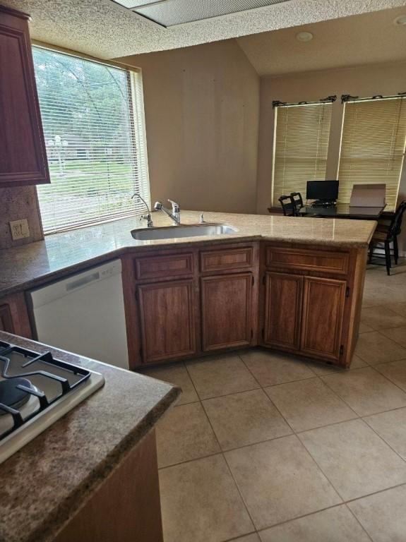 kitchen featuring light tile patterned floors, stainless steel gas cooktop, a sink, a textured ceiling, and dishwasher