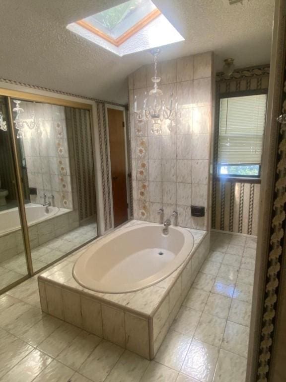 full bathroom with a garden tub, vaulted ceiling with skylight, a textured ceiling, and wallpapered walls