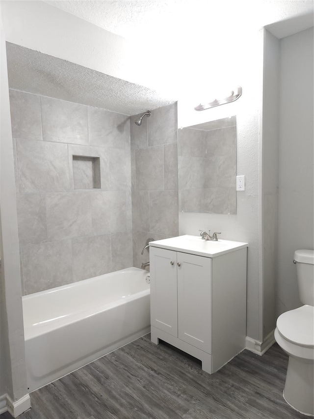 full bathroom with tiled shower / bath combo, a textured ceiling, toilet, vanity, and hardwood / wood-style flooring