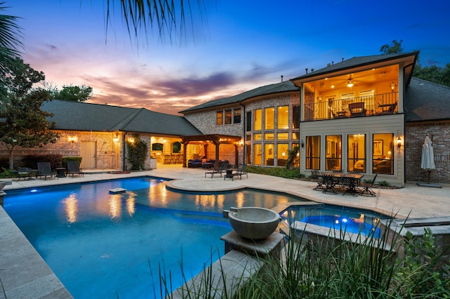 pool at dusk featuring ceiling fan and a patio area