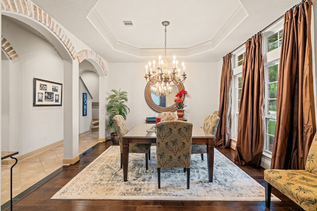 dining space with crown molding, a raised ceiling, dark wood-type flooring, and an inviting chandelier