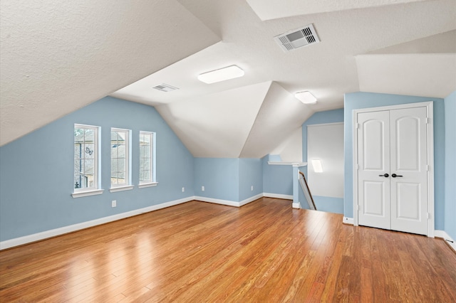 additional living space featuring a textured ceiling, light wood-type flooring, and lofted ceiling