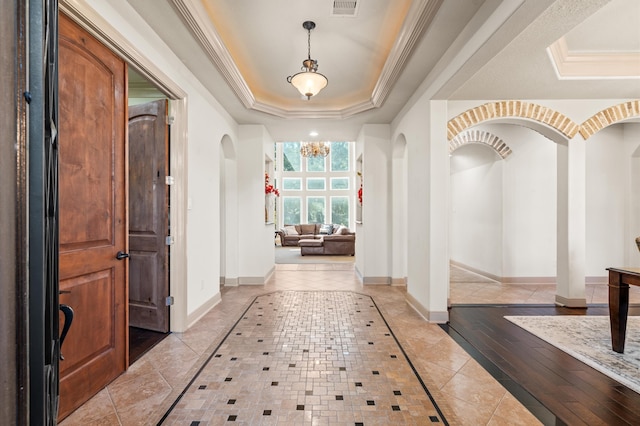 hall with light hardwood / wood-style floors, a tray ceiling, crown molding, and a notable chandelier