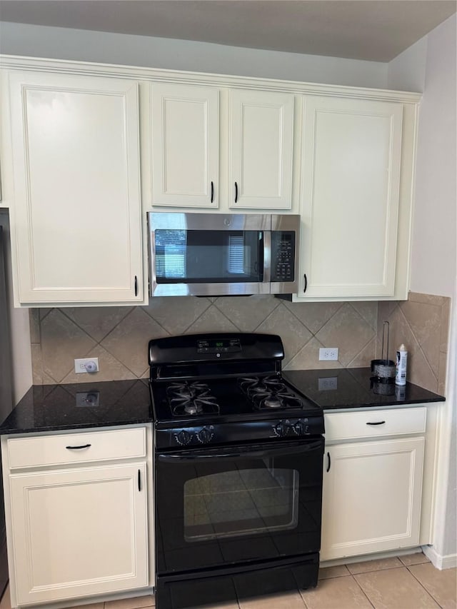 kitchen with white cabinets, gas stove, dark stone countertops, backsplash, and light tile patterned flooring