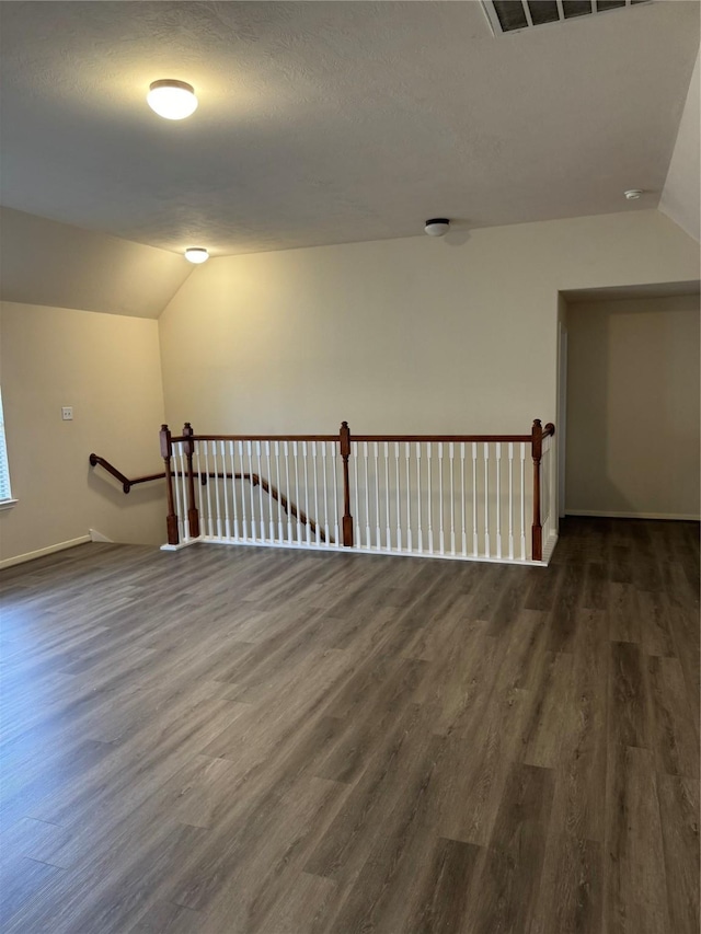 unfurnished room with vaulted ceiling, dark hardwood / wood-style floors, and a textured ceiling