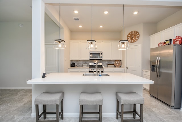 kitchen with backsplash, hanging light fixtures, a kitchen island with sink, white cabinetry, and appliances with stainless steel finishes