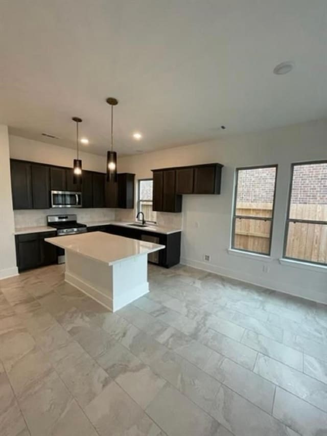 kitchen with pendant lighting, sink, a kitchen island, dark brown cabinetry, and stainless steel appliances