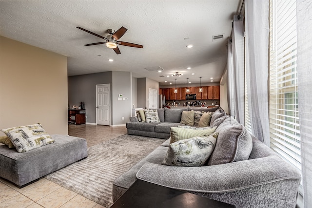 living room with a textured ceiling, ceiling fan, and light tile flooring