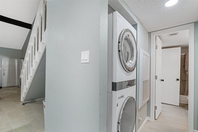 laundry room with a textured ceiling, stacked washing maching and dryer, and light tile patterned flooring