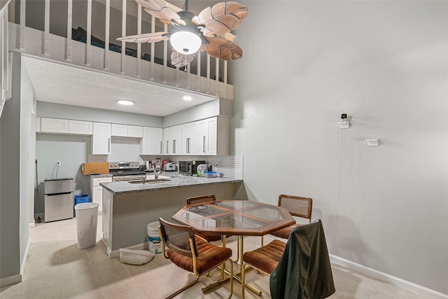 kitchen with white cabinetry, light stone counters, backsplash, kitchen peninsula, and appliances with stainless steel finishes