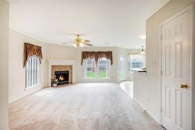 unfurnished living room with a tiled fireplace, light carpet, and ceiling fan