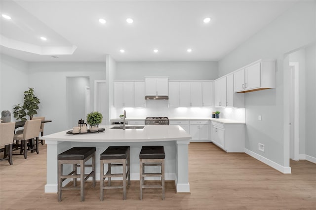 kitchen featuring white cabinetry, sink, an island with sink, a kitchen bar, and range