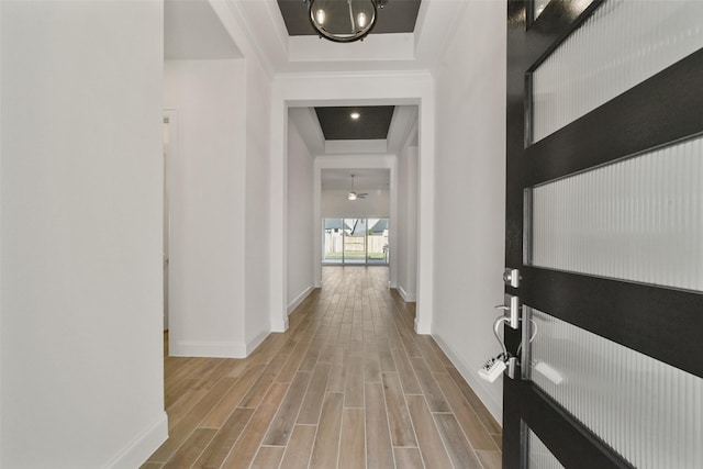 corridor with a tray ceiling and light hardwood / wood-style floors